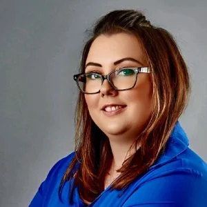 woman smiling with glasses and a blue shirt with a solid grey background
